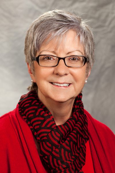 portrait photo of Carol Ann Pacco-Long, a woman wearing a red sweater with a black and red patterned scarf