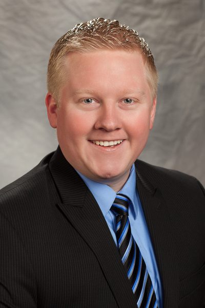 portait photo of Alvey Harrison, a man wearing a black suit, a blue button down shirt, and a striped tie