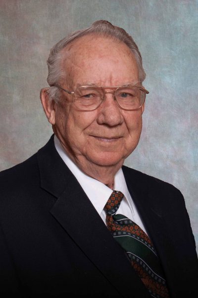 portait photo of Don Briner, a man with glasses wearing a black suit jacket, white shirt, and orange and green tie