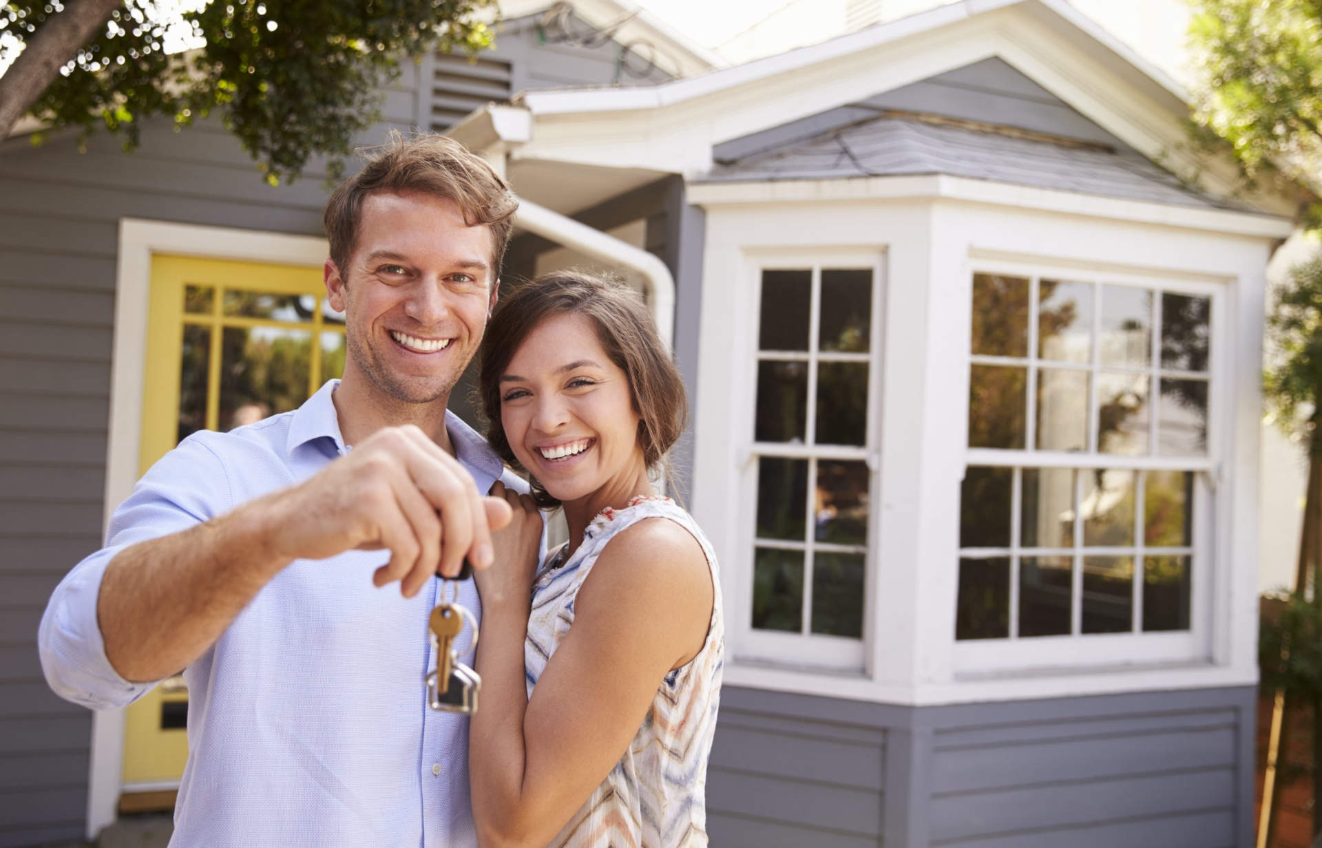 first-time homebuyers standing in front of their new home after deciding on whether a 15-year or 30-year mortgage is better