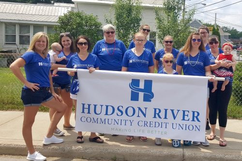 group photo from 4th of July parade with HRCCU ambasaddors dressed in blue HRCCU shirts carrying a large banner