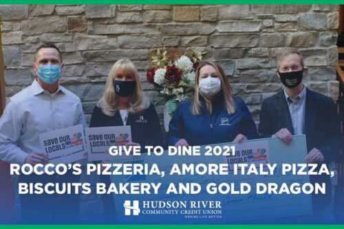 four adults standing in front of a stone wall holding a check donated to the Give to Dine program