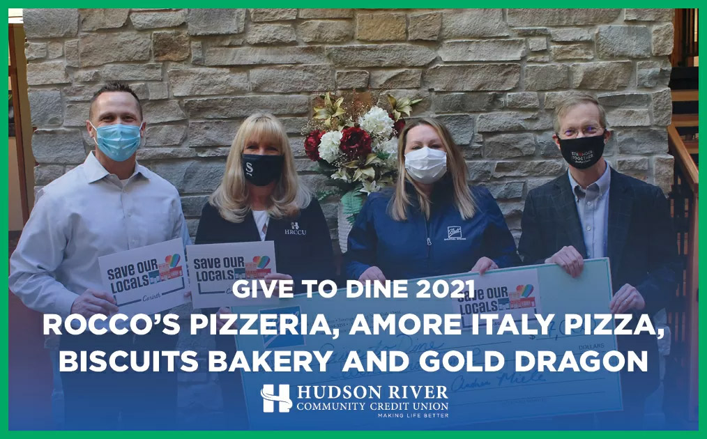 four adults standing in front of a stone wall holding a check donated to the Give to Dine program