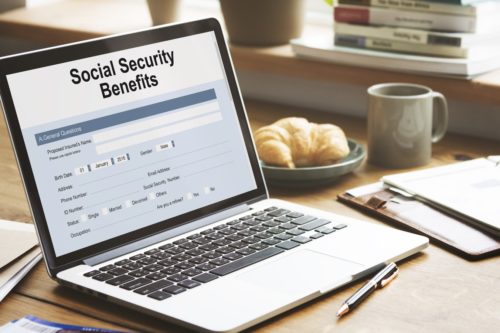 silver laptop with a Social Security benefits form on the screen on a wooden table