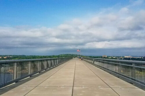 Walkway Over the Hudson walking bridge on a sunny day with white clouds in the sky and an American flag marking the halfway point of the bridge