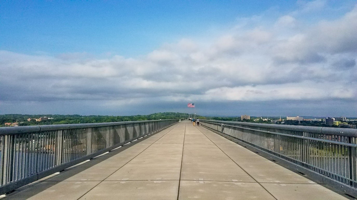 Walkway Over the Hudson walking bridge on a sunny day with white clouds in the sky and an American flag marking the halfway point of the bridge