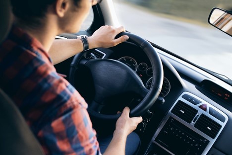 closeup of an adult wearing a red and blue plaid shirt driving a vehicle with a black steering wheel