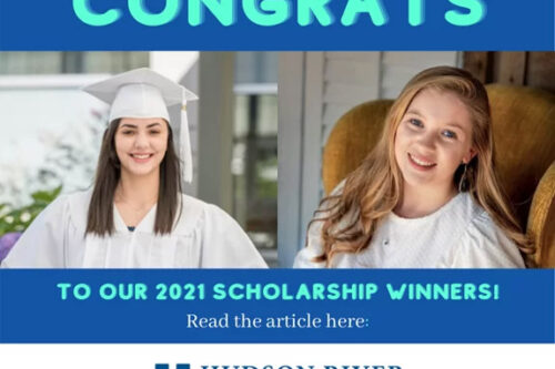young woman with brown hair wearing a white graduation cap and gown next to a young woman with red hair sitting in a brown armchair