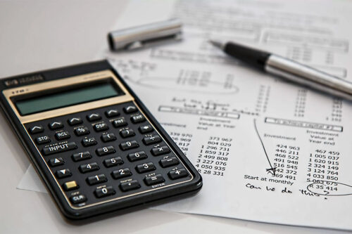 closeup of black calculator next to silver pen with black gripper on a white budget sheet with black text