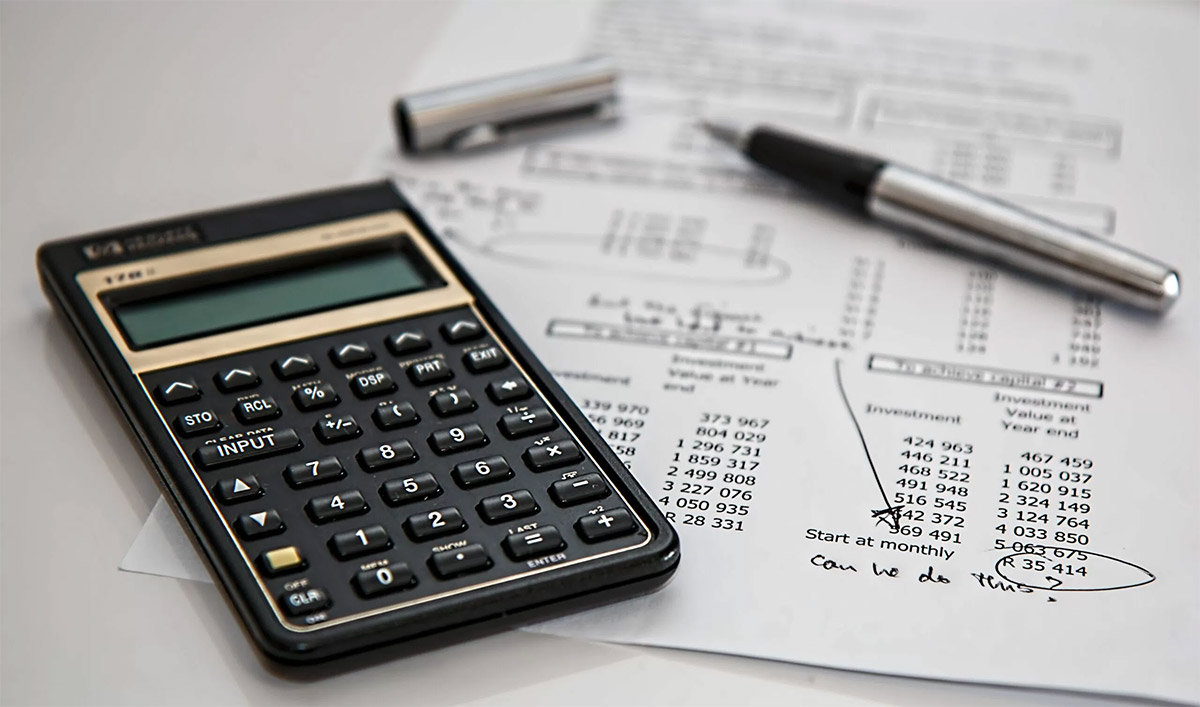closeup of black calculator next to silver pen with black gripper on a white budget sheet with black text