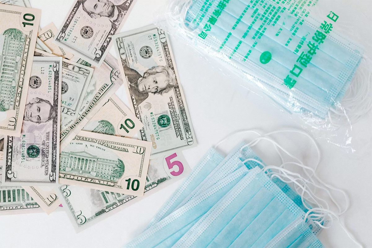 overhead shot of green-colored United States currency for a health savings account next to blue face masks on white table