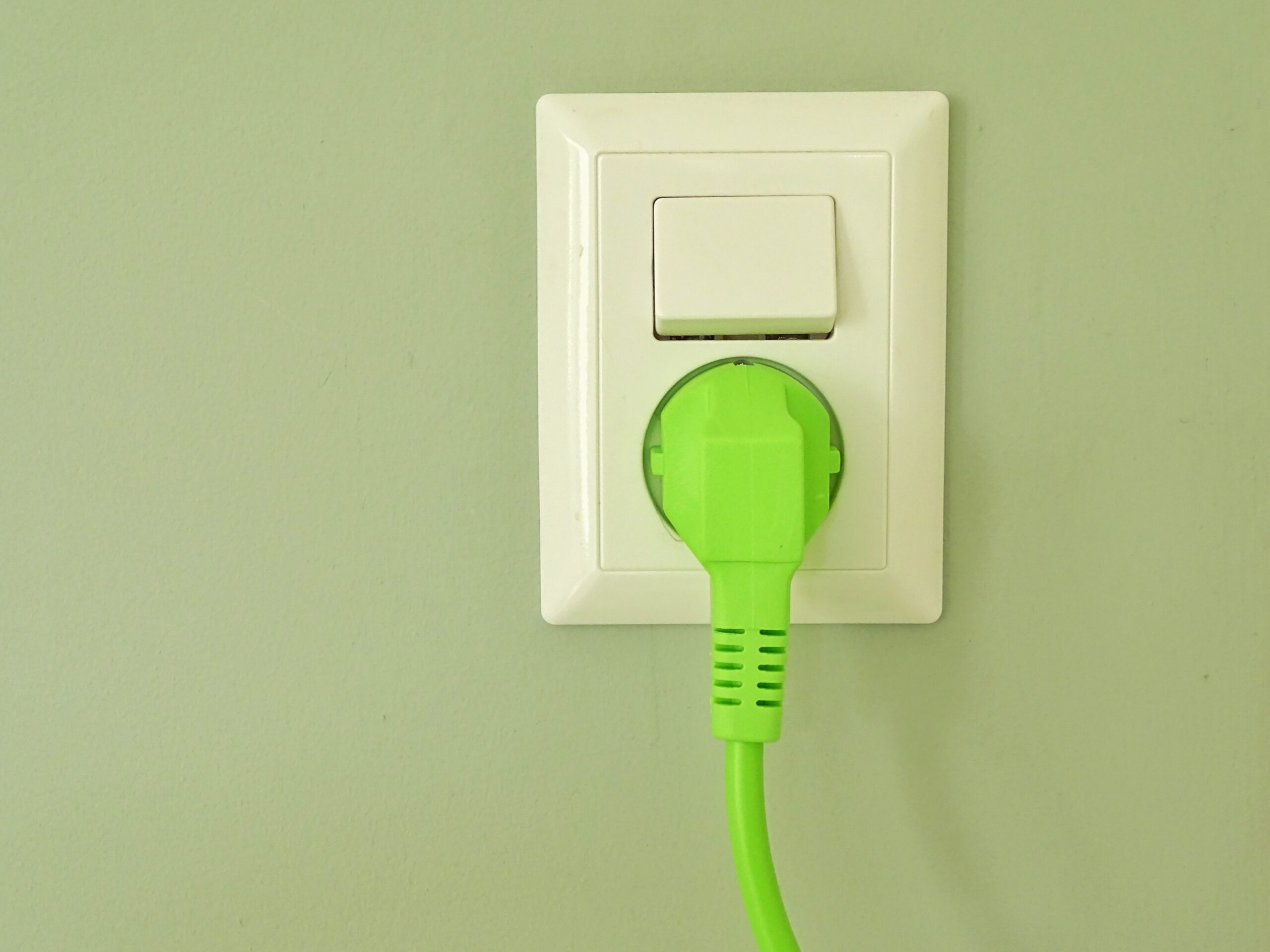 white-colored power outlet with a bright green plug mounted on green wall