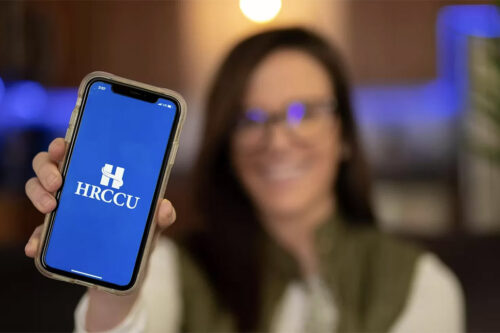 brunette HRCCU mobile banking and budgeting app user holding up iPhone with the blue HRCCU logo on it