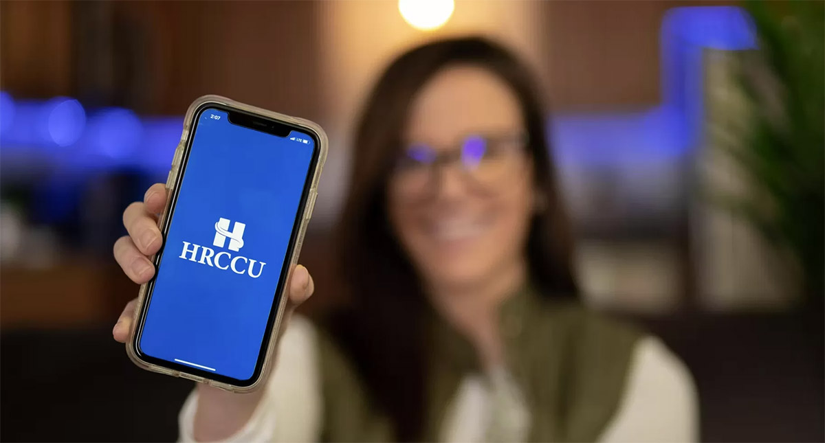 brunette HRCCU mobile banking and budgeting app user holding up iPhone with the blue HRCCU logo on it