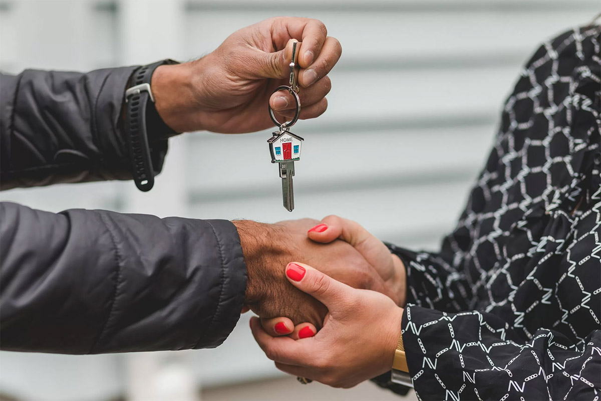 woman with red nail polish on her fingers wearing a black shirt with a white pattern shaking the hands of a man wearing a black coat, holding house keys