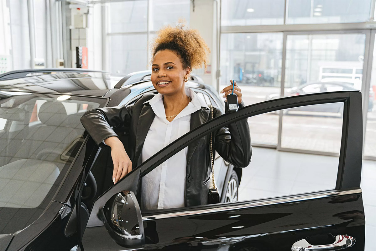 woman with her hair pulled back wearing a black coat standing behind the driver’s side door of a black car