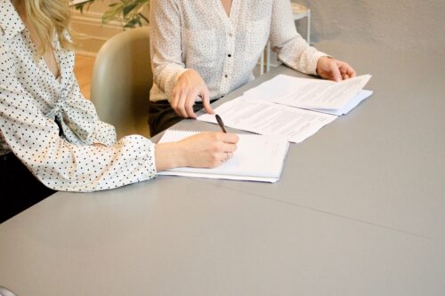 two women sitting at a gray conference table reviewing financial paperwork
