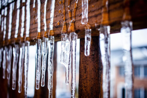 ice and snow melting on the beams of a wooden deck next to a house