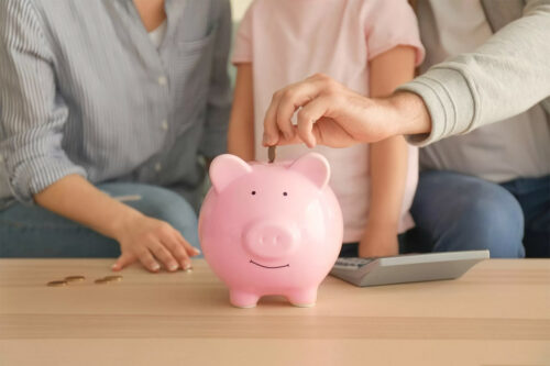 Little girl with her parents putting coins into piggy bank indoors. Money savings concept