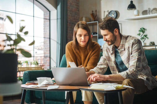 Couple Using Laptop Computer, Sitting on Sofa in Apartment