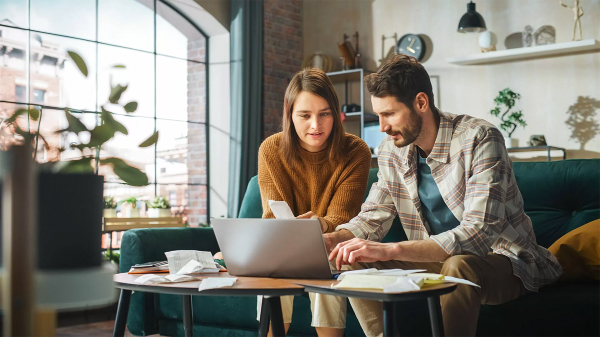 Couple Using Laptop Computer, Sitting on Sofa in Apartment