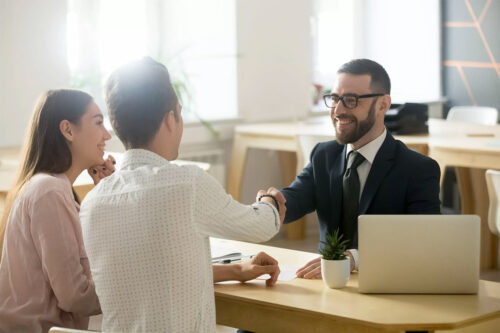 young banker shakes hands with young couple over desk