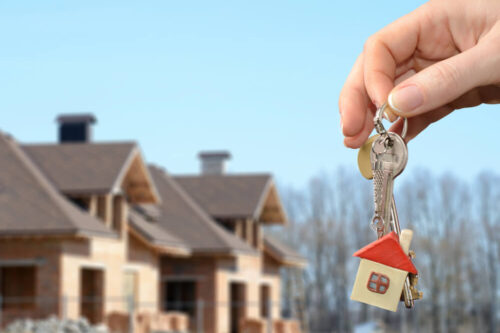 homes under construction in the background with a hand holding a set of keys with a house key ring