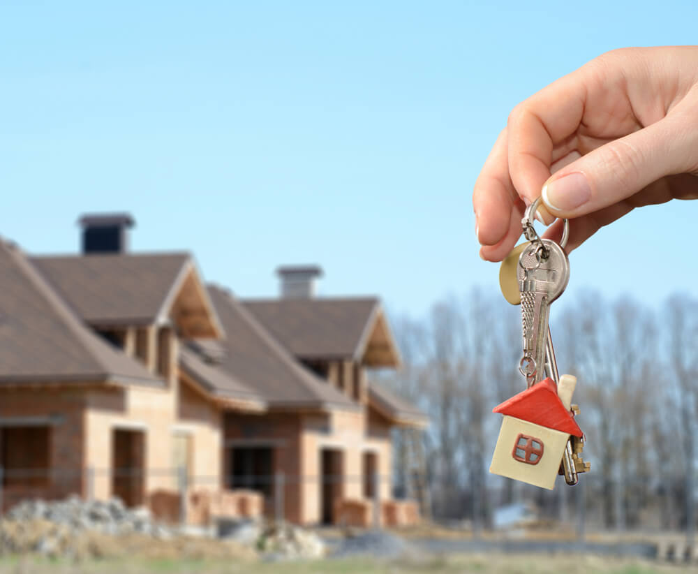homes under construction in the background with a hand holding a set of keys with a house key ring