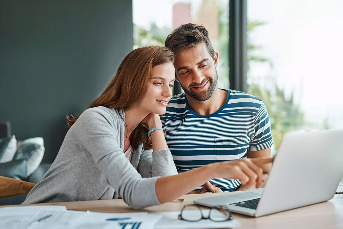 A couple sitting down at a lap top with files and paperwork for their home insurances on the table