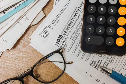 glasses, tax papers, and a calculator sit upon a desk as the tax season begins to roll around