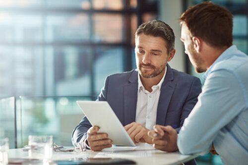 Two men sit at a table with banking sheets planning financial wellness