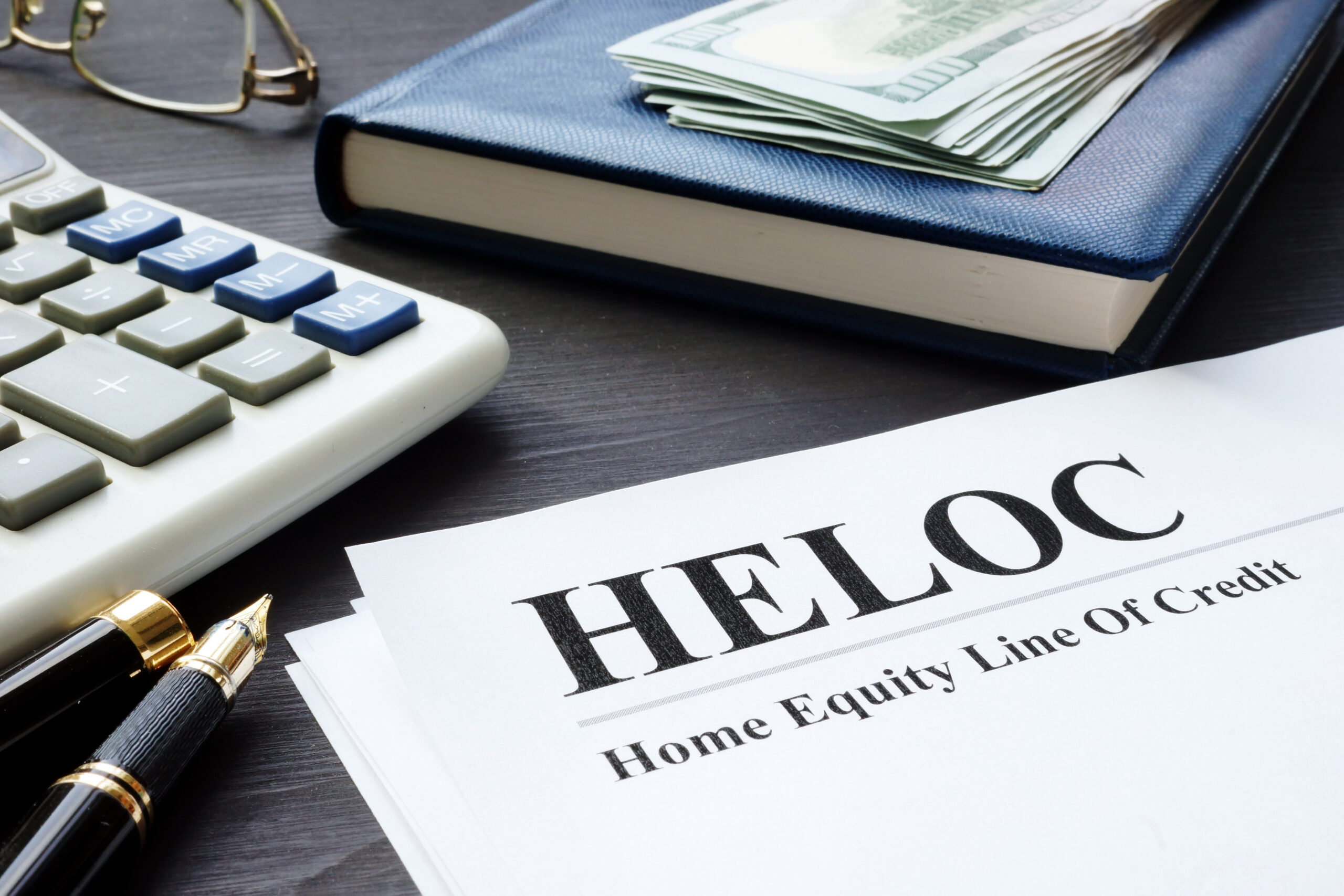 A HELOC agreement sits on a dark table with a calculator and checking books nearby