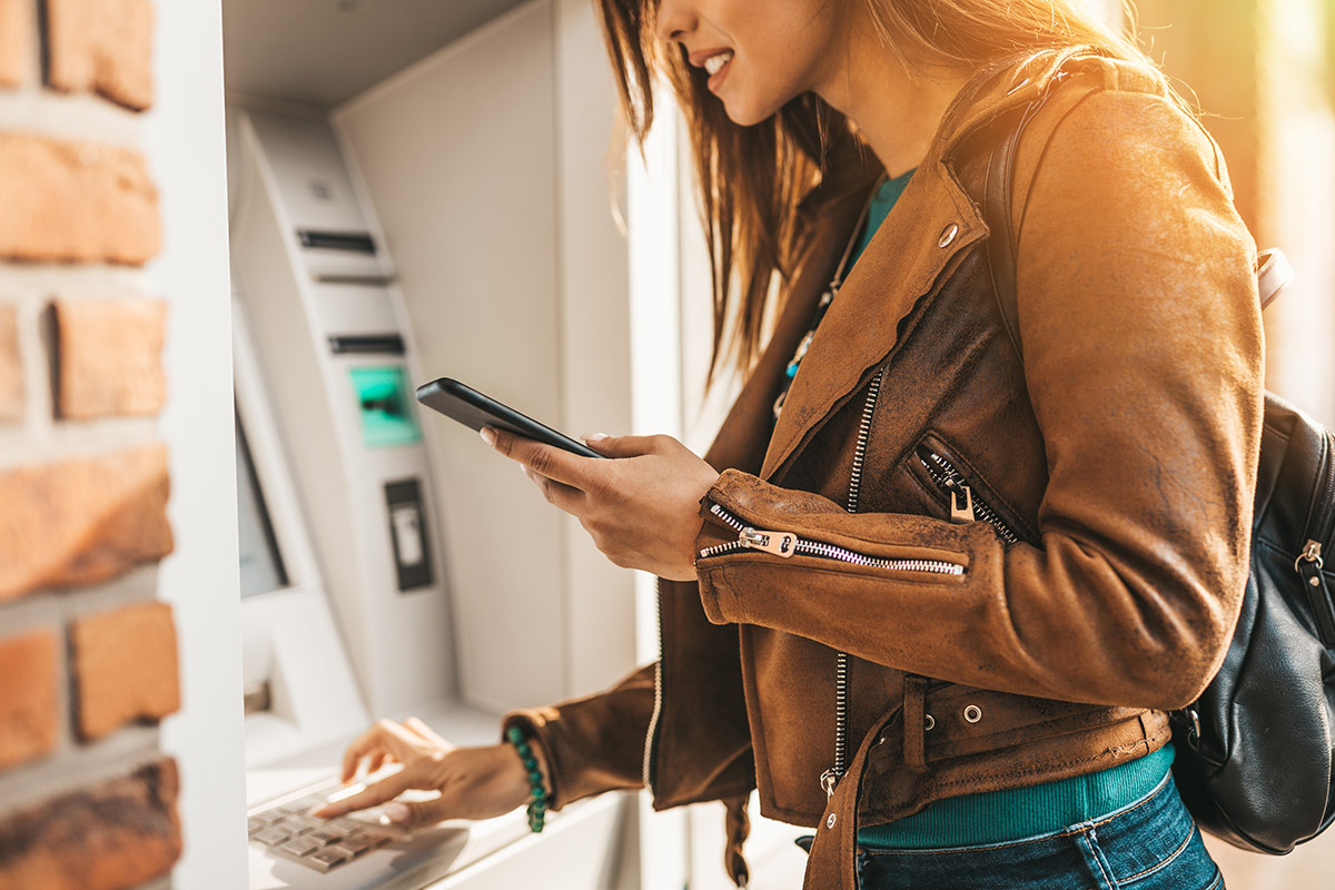 woman using atm with phone in hand