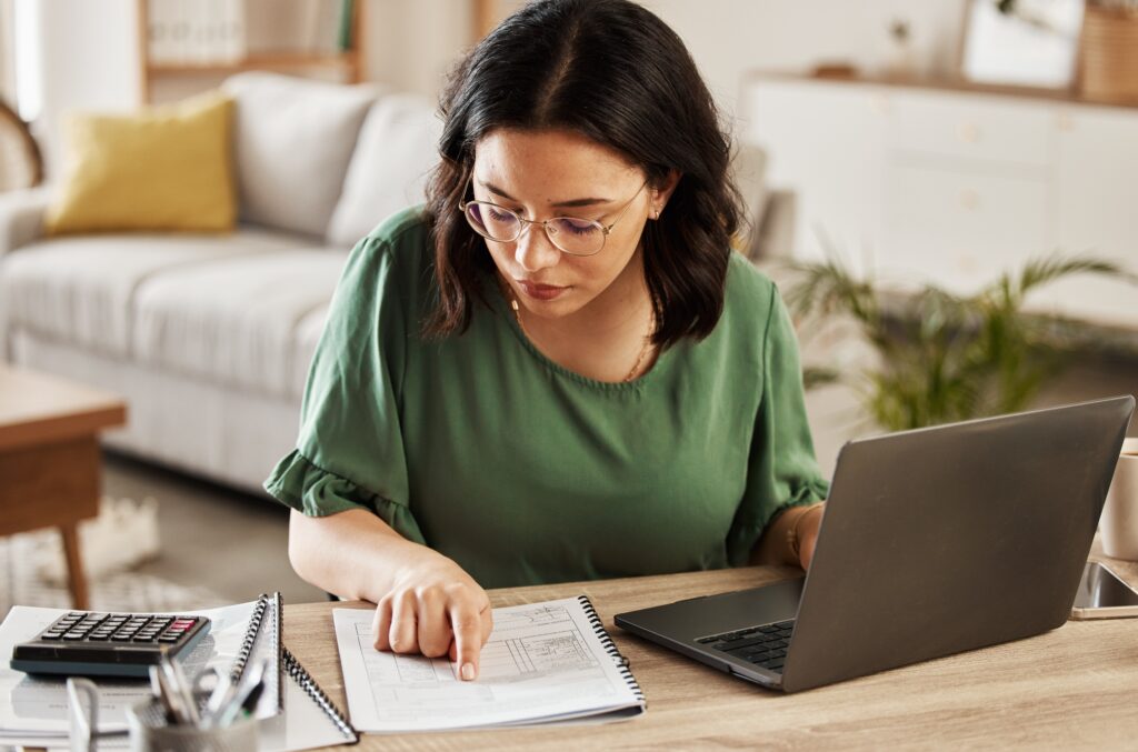 Woman sitting at the counter with a laptop and calculator determining a zero based budget
