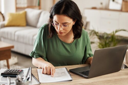 Woman sitting at the counter with a laptop and calculator determining a zero based budget